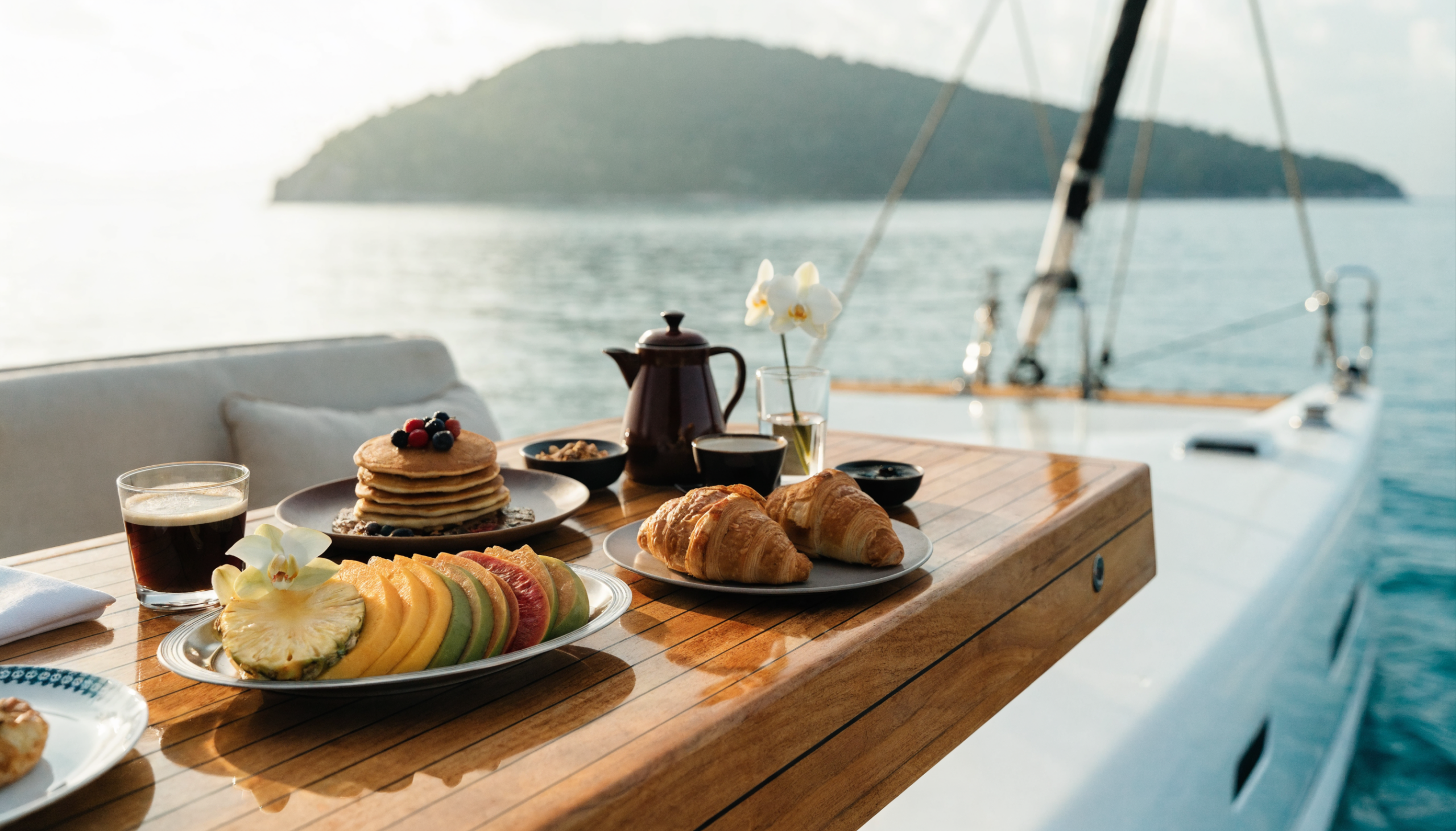 A private chef's breakfast spread laid out on the teak deck of a catamaran at anchor